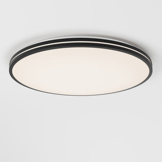 The Artika Athos 21 in. LED flush mount light features a modern round design with a black rim and smooth frosted white surface, seamlessly mounted on a white ceiling, and comes with a remote for easy control.