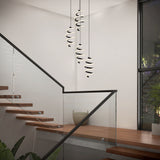 Modern indoor staircase with wooden steps and glass railing. Three spiral pendant lights hang from the ceiling. There’s a large window, a potted plant, and a decorative vase on a landing. The setting is bright and minimalistic.