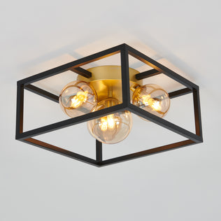 The Artika Griffintown flush mount is a modern ceiling light with exposed bulbs, a black open square metal frame, and a brass base, installed on a white ceiling.