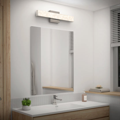 A modern bathroom features an Artika Adeline modern LED bathroom vanity light 3 CCT above a large mirror, complemented by a sleek sink, potted plant, soap dispenser, folded towels, and natural light through window blinds.