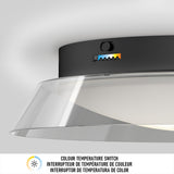 Close-up of a black ceiling light fixture with a transparent shade, featuring a color temperature switch and indicator with five color settings. Text below describes the switch in English, French, and Spanish.