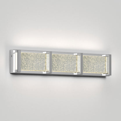 The Artika Subway Essence 3 LED bathroom vanity light features three rectangular sections with chrome accents and frosted glass panels filled with sparkling bubble details, mounted on a plain light gray wall.