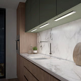 Modern kitchen with marble backsplash and countertop, wooden cabinets, a sleek built-in oven, under-cabinet lighting, a contemporary faucet, a small green plant, and kitchen accessories near the sink.