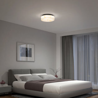 A modern bedroom with a gray upholstered bed, white bedding, a dark gray throw, nightstand, wall art, large window with sheer curtains, and an Artika Clifford 15 in. flush mount light softly illuminating the room.