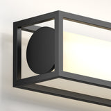 A close-up of a modern rectangular wall light fixture with a black metal frame, featuring a round black accent on the side and a glowing white light panel inside.