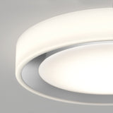 Close-up of a modern, circular ceiling light with a white, smooth surface, softly glowing and creating a gentle, diffused illumination against a light gray background.